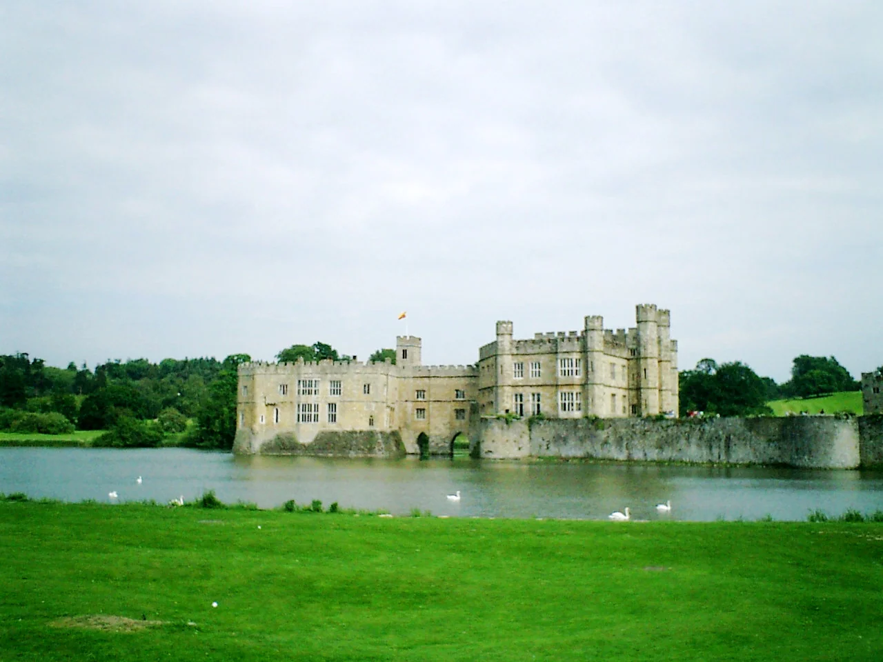 陰天湖畔遠望 Leeds Castle，前方有草地與湖水。