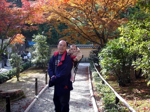 爸爸用背架背著小孩，站在紅葉步道前。