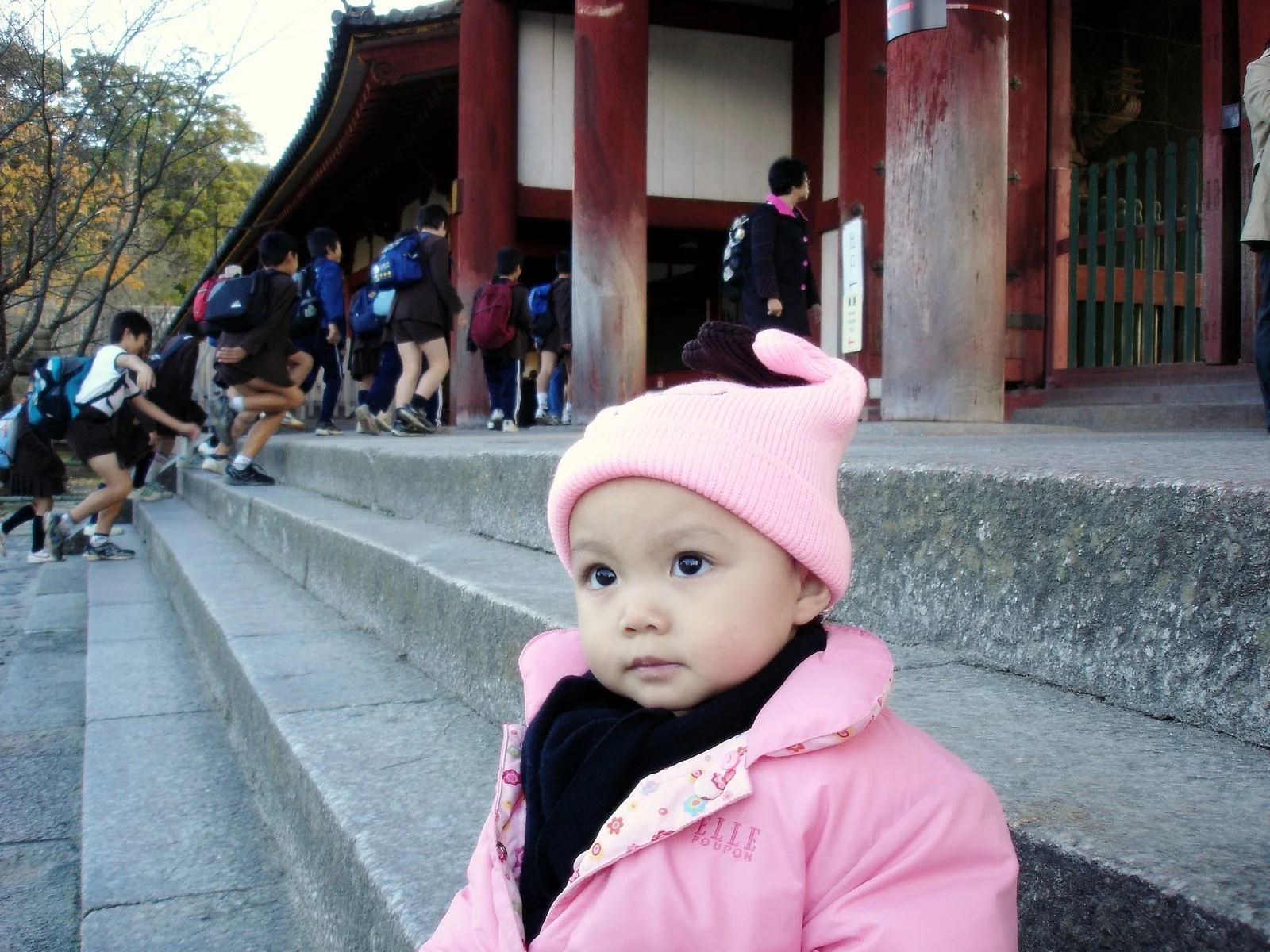 小孩戴粉紅色帽子坐在寺院台階旁。