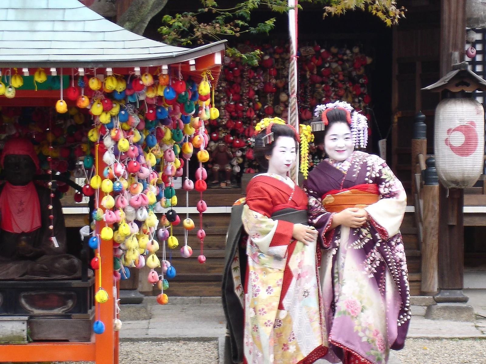 兩位穿和服的藝妓站在京都街邊小寺社旁。