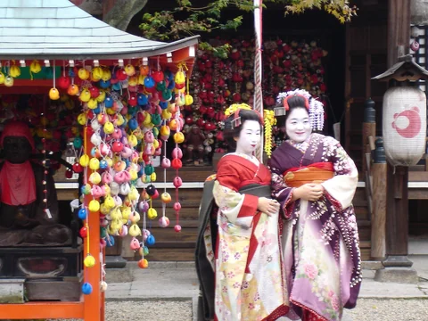 兩位穿和服的藝妓站在京都街邊小寺社旁。