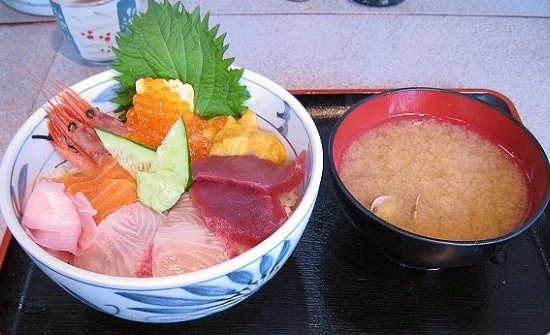海鮮丼旁放著味噌湯，丼飯上有生魚片、海膽與鮭魚卵。