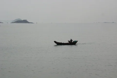 灰濛海面上一艘小船行駛，遠方可見島影。